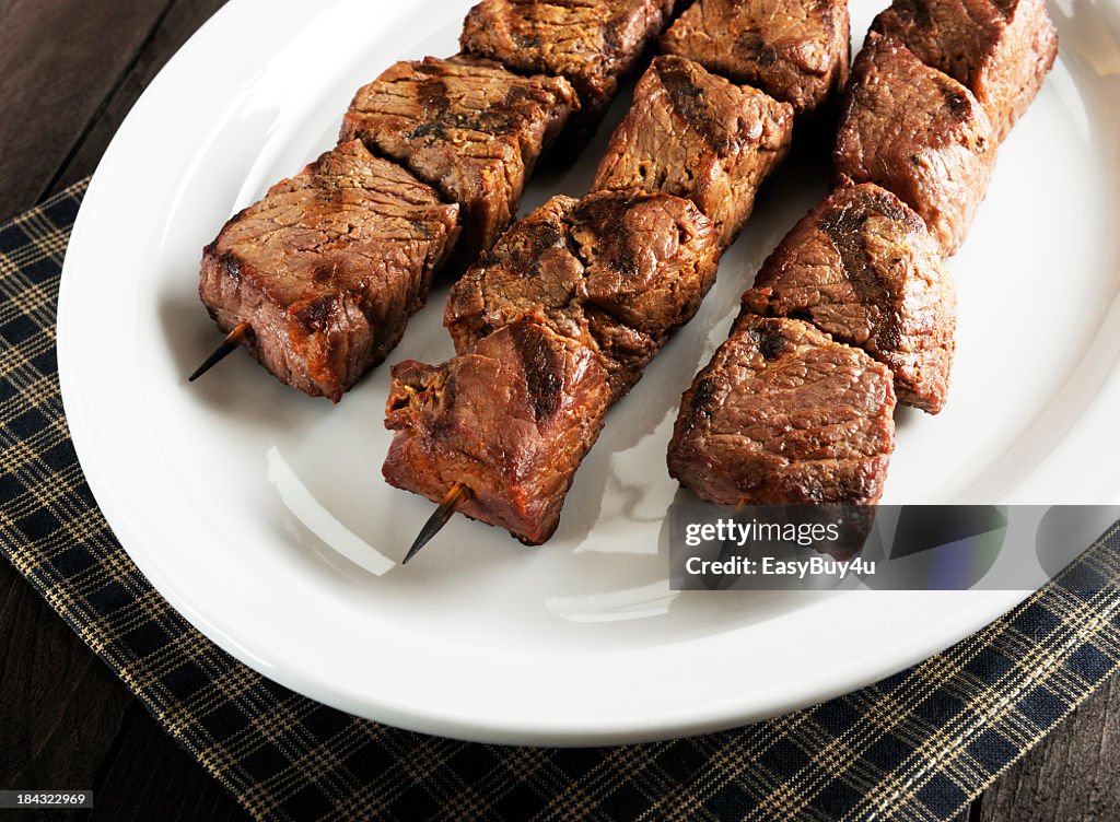 Three beef kebabs arranged on a white platter