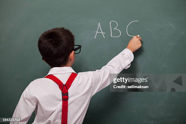 backview of little boy writing alphabet on green blackboard - b stock pictures, royalty-free photos & images