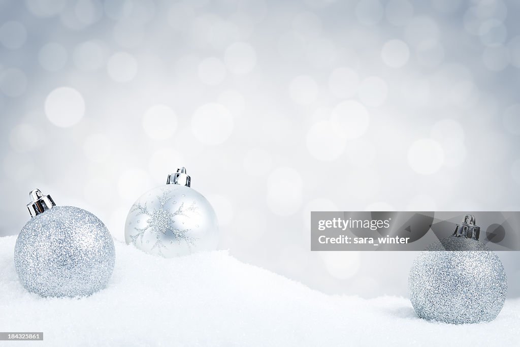 Silver Christmas baubles on snow with a silver background