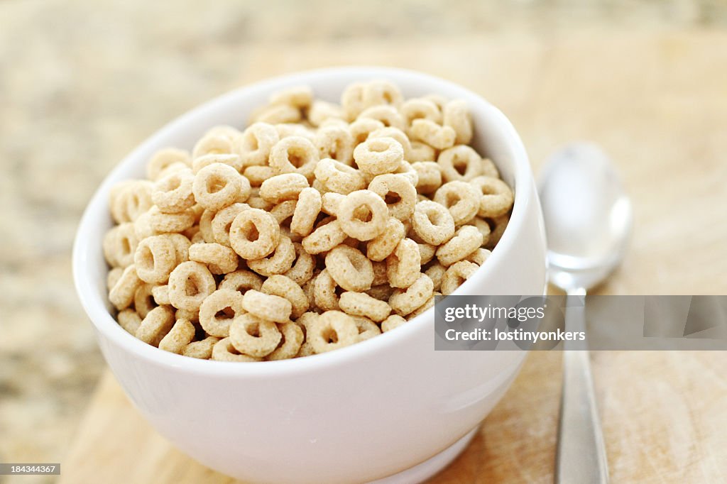 Oat cereal in loop shape in white bowl with spoon next to it