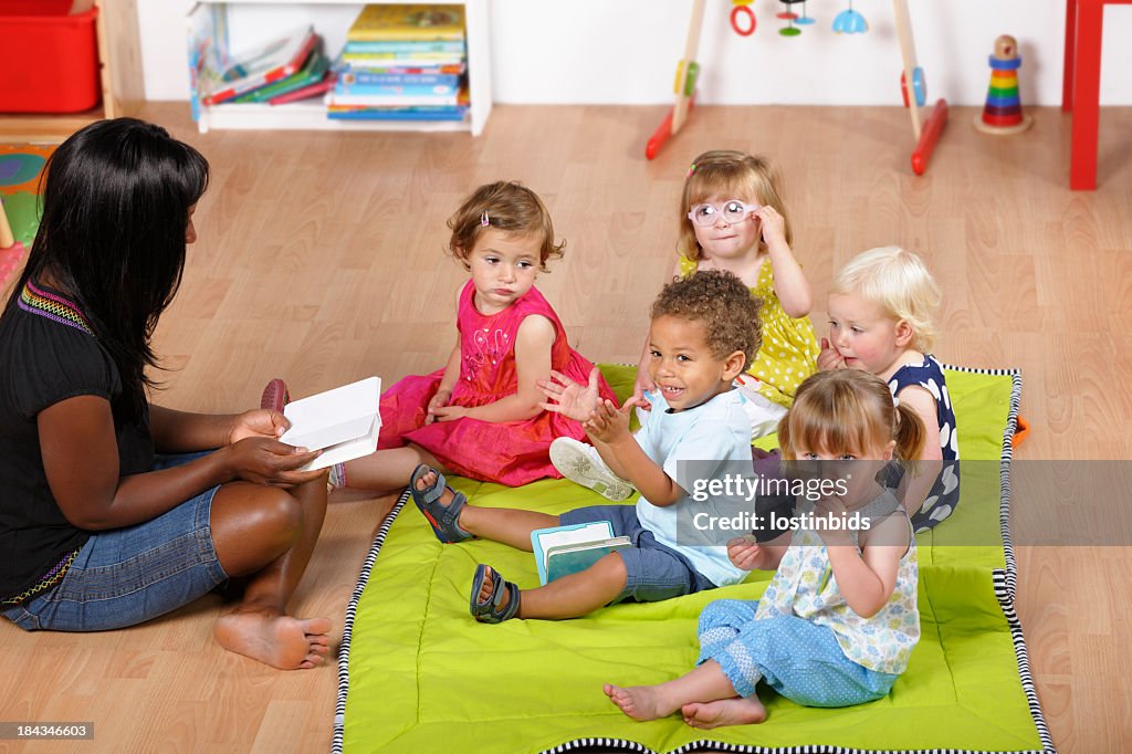 Childminder Reading To A Group Of Toddlers At Nursery