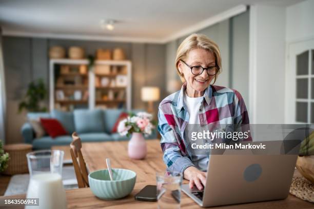 a mature woman enjoys her morning and a non-working day in her modern apartment - pleased face laptop stock pictures, royalty-free photos & images