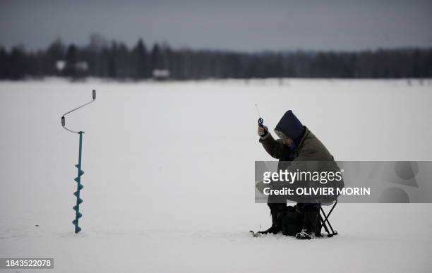 Man fishes through the ice after digging a hole in a frozen river on December 17, 2008 in Rovaniemi. In this region the ice is about 20 centimeters...