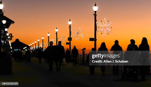 Huntington Beach, CA 80 snowflakes light up the Huntington Beach Pier as pier walkers are silhouetted by the sunset's glow amid pleasant weather in...