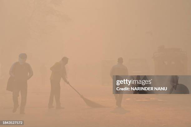 Man sweeps along a street as people walk amid heavy smog in Amritsar on December 13, 2023.