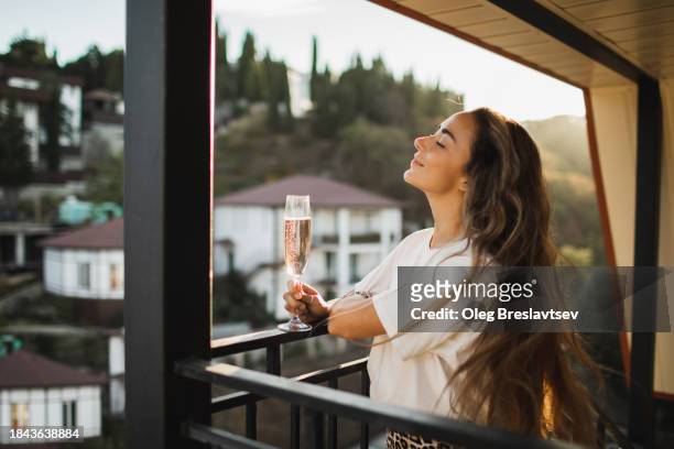 woman relaxing on terrace with glass of cold champagne. celebration concept, pleasure and positive emotions. - cipresso stock-fotos und bilder