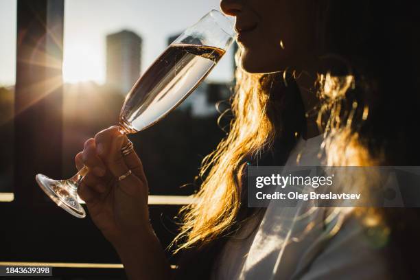 close-up champagne flute in hand, woman drinking alcohol drink at sunset - cipresso stock-fotos und bilder