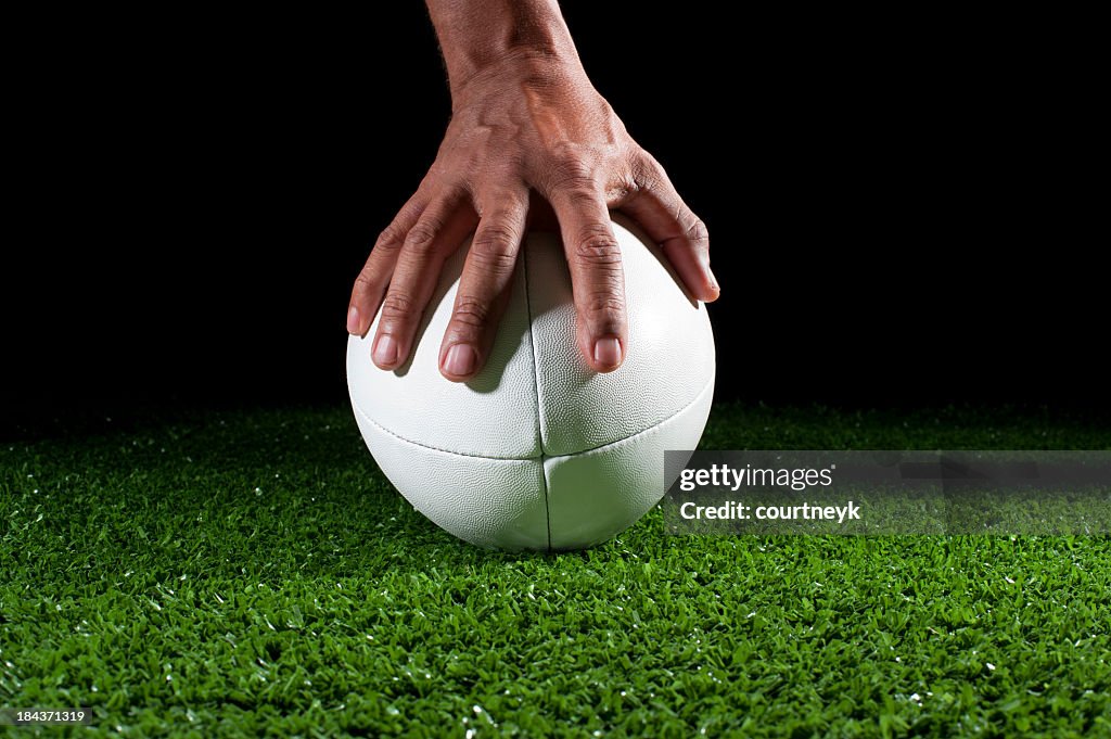 White rugby ball with hand holding it in grass