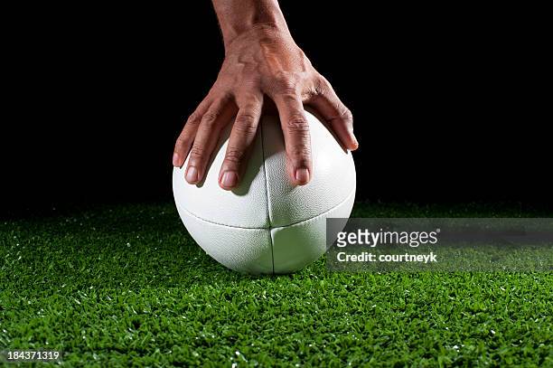 white rugby ball with hand holding it in grass - rugby ball stockfoto's en -beelden