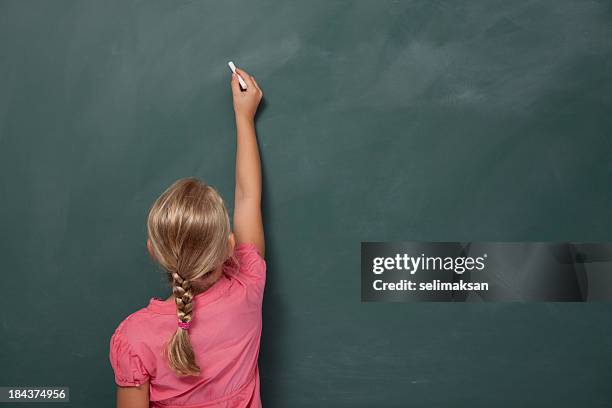 back view of little girl writing on blank blackboard - schoolbord stockfoto's en -beelden