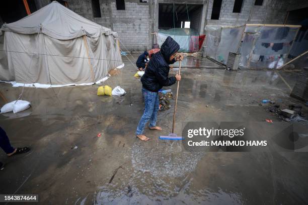 Palestinian boy attempts to get water out after raining at a camp for displaced people in Rafah, in the southern Gaza Strip where most civilians have...