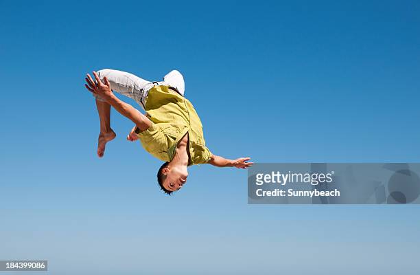 man doing somersault in the air against blue sky - flip over stockfoto's en -beelden