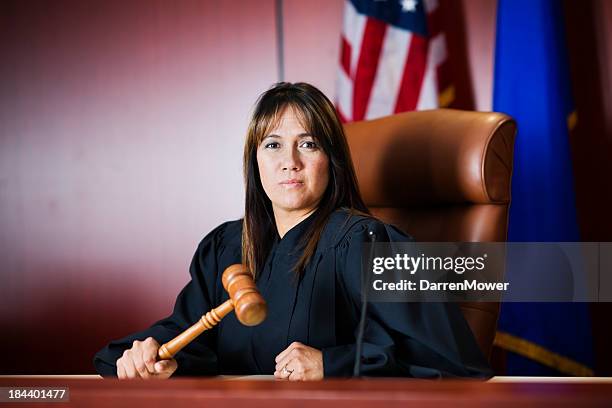 female judge sitting in court holding her gavel - judge stockfoto's en -beelden