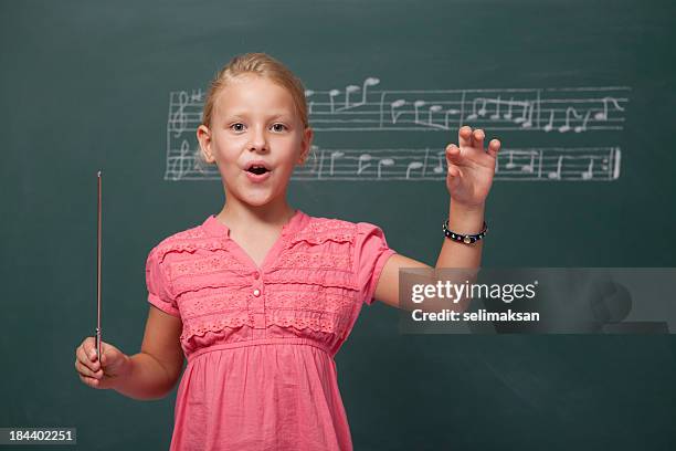 little girl directing chorus for folk music before blackboard - dirigeerstok stockfoto's en -beelden
