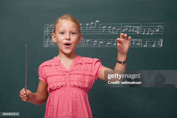 little girl directing chorus for folk music before blackboard - dirigent stockfoto's en -beelden