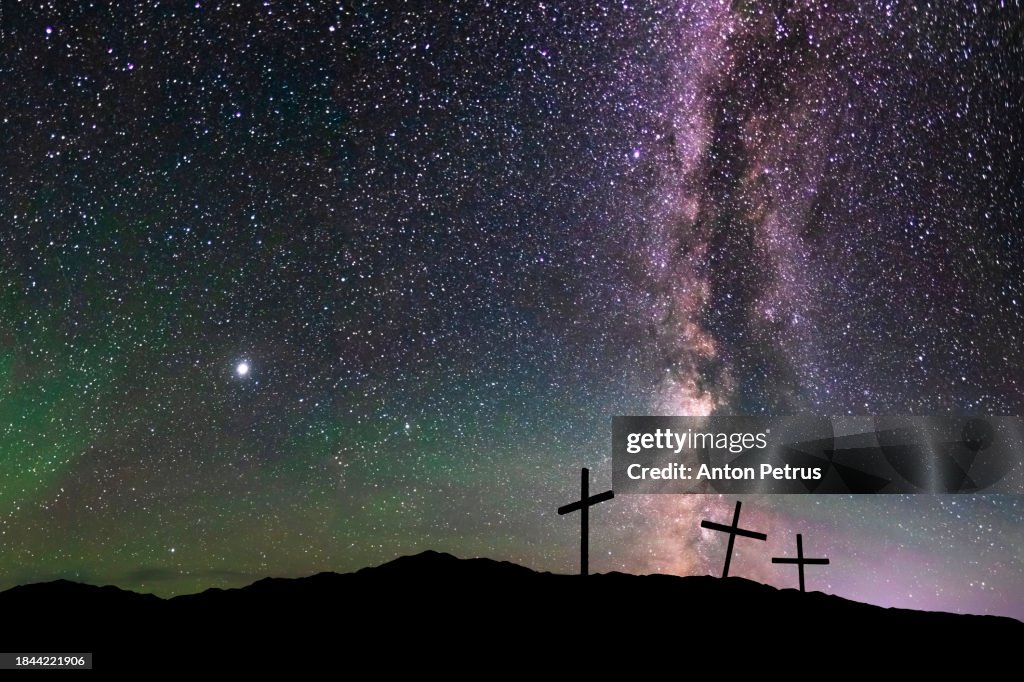 Three Christian crosses on a hill at night under the starry sky