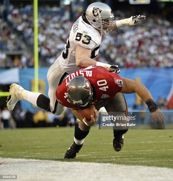 Mike Alstott of the Tampa Bay Buccaneers carries the ball as he is pushed out of bounds by an airborne Bill Romanowski of the Oakland Raiders during...