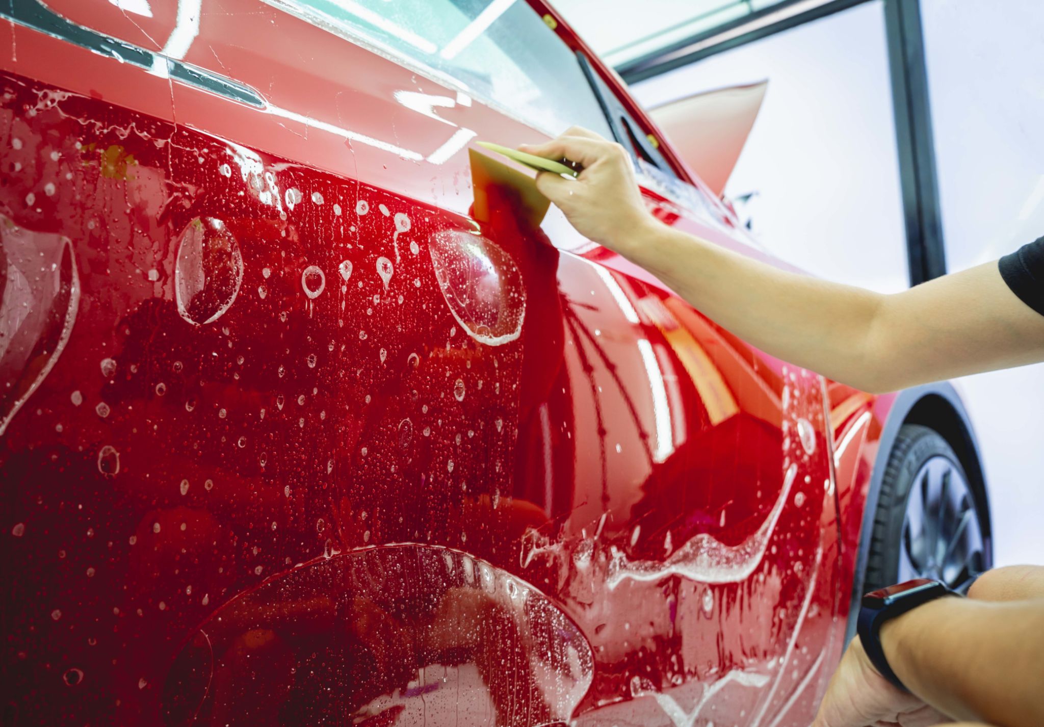 The process of installing protective film on the new red car. The process of installing protective film on the new red car.