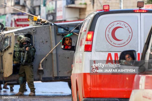 An Israeli soldier aims his weapon as Palestinian Red Crescent ambulances wait on December 13 following an overnight army raid in Jenin in the...