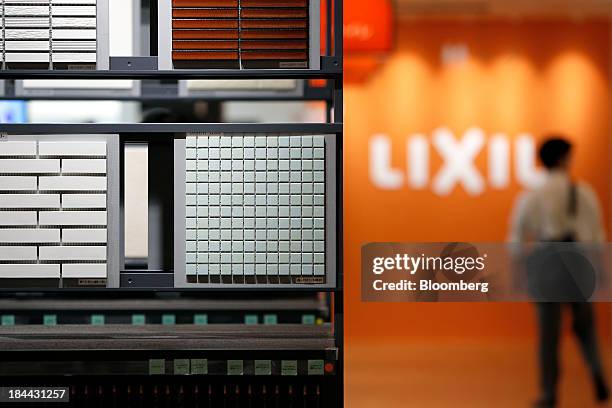 Samples of interior wall tiles, left, are displayed in front of the Lixil Corp. Logo at the company's showroom in Tokyo, Japan, on Friday, Oct. 11,...