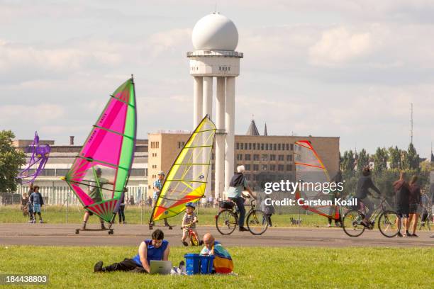 Man sits with a laptop on the ground as enthusiasts exercis wind skating on a longboard with a mounted sail across a runway at former Tempelhof...