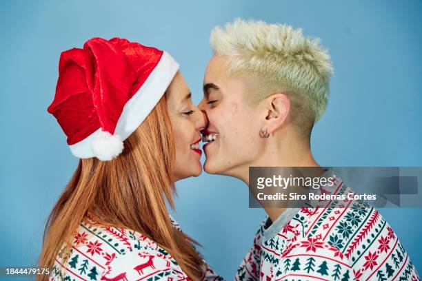 two lesbian women kiss at home on christmas. - gay santa claus stock-fotos und bilder