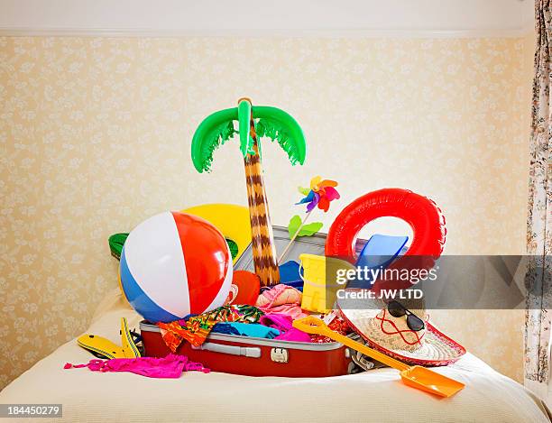 suitcase full of inflatable holiday props on bed - hat sombrero stock pictures, royalty-free photos & images