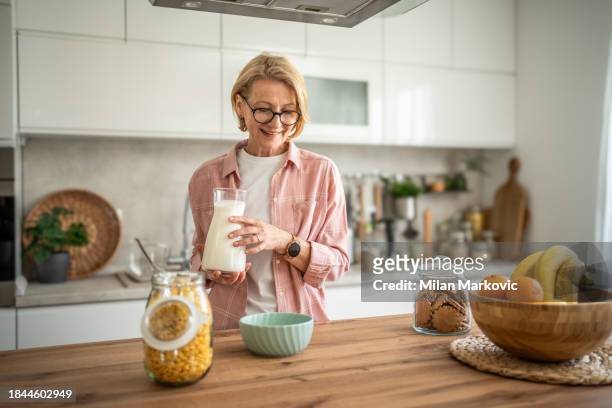 eine ältere frau bereitet ein gesundes frühstück zu, cornflakes mit milch - 50 60 jahre brille stock-fotos und bilder