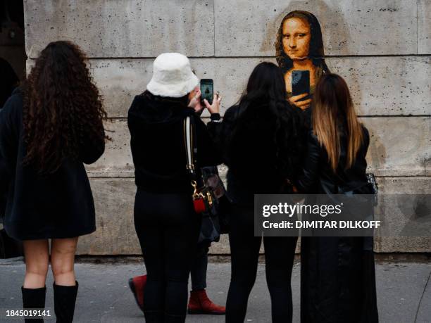 Women take photos with their mobile phones of a street art poster, made by French artist Big Ben, depicting Leonardo da Vinci's Mona Lisa holding a...