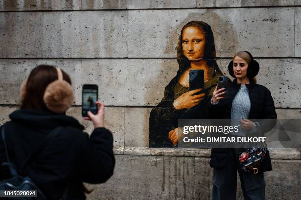 Women take photos with their mobile phones of a street art poster, made by French artist Big Ben, depicting Leonardo da Vinci's Mona Lisa holding a...