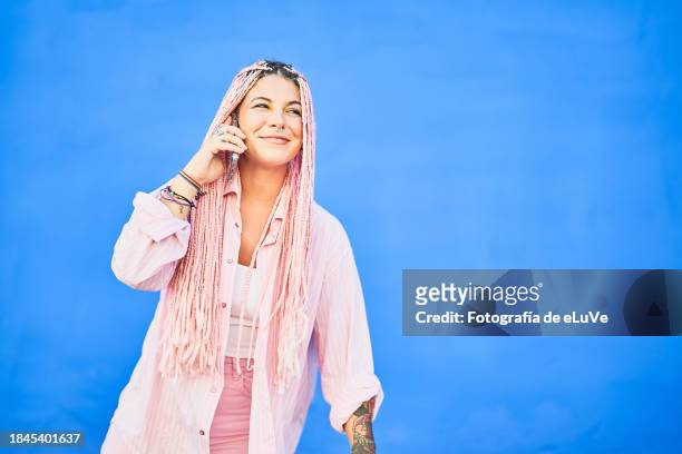 chica joven feliz hablando por teléfono sobre un fondo azul al aire libre - teléfono stock pictures, royalty-free photos & images