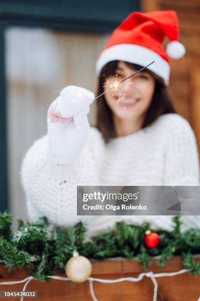 sparkler celebration on christmas: woman in santa hat, brandishes a sparkler in christmas decorations. focus on hand with bengal fire - bengalischer feuer stock-fotos und bilder