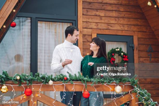 sparkling celebration for couple on getaway: couple with sparklers celebrating christmas on the veranda of a log cabin during their glamping adventure. - bengalischer feuer stock-fotos und bilder