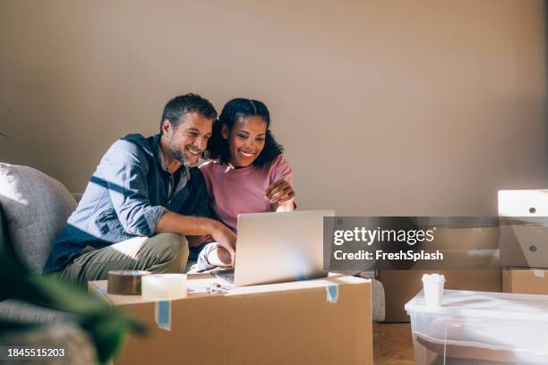 happy couple using a laptop while moving in - unpacking stock pictures, royalty-free photos & images