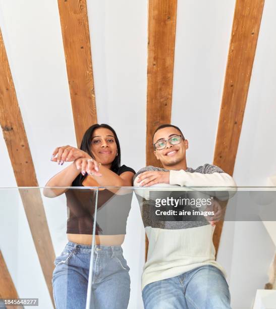 an embracing young couple looking down from a balcony with glass railings and smiling at each other - private terrace balcony stock pictures, royalty-free photos & images