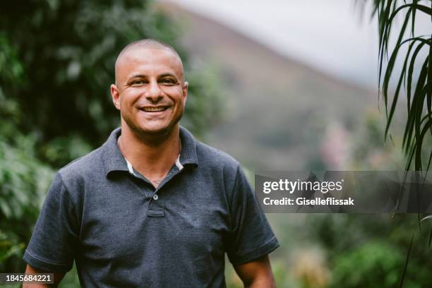 smiling man standing outside on a his patio with a scenic view - kaal geschoren hoofd stockfoto's en -beelden