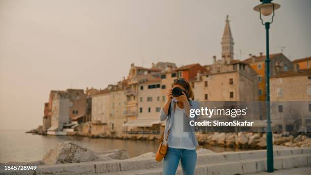 female tourist photographing at camera against old town in rovinj during vacation in croatia - travel photographer stock pictures, royalty-free photos & images