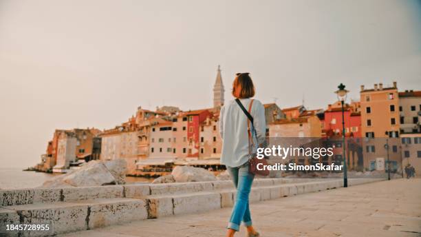 rear view of female tourist walking on pier while looking old town in rovinj in croatia - crossbody bag stock pictures, royalty-free photos & images