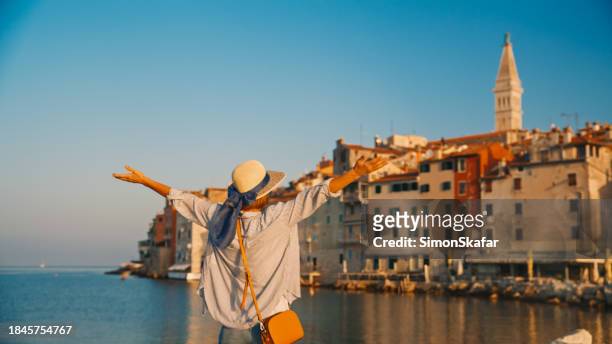 rear view of female tourist standing with arms outstretched against old town in rovinj by sea and clear blue sky during summer at croatia - rovinj stock pictures, royalty-free photos & images