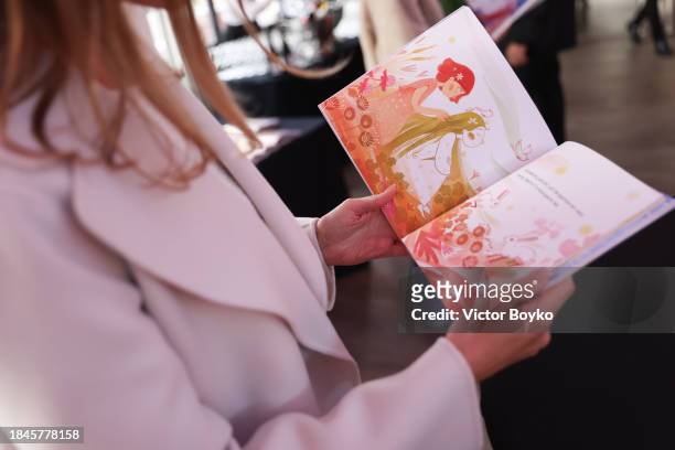 Guest is browsing a "My home" book by Angelina Usanova at the charity event hosted by Miss Universe Ukraine 2023 Angelina Usanova on December 10,...