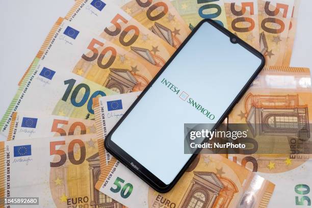 The Intesa Sanpaolo logo is being displayed on a smartphone screen that is placed on 50 and 100 Euro bills in Athens, Greece, on December 13, 2023.