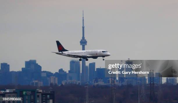 An Air Canada airplane flies in front of the downtown skyline and CN Tower as it lands at Pearson International Airport on December 10 in Toronto,...