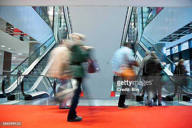 blurred people walking red carpet to escalator in modern interior - red carpet stairs stock pictures, royalty-free photos & images
