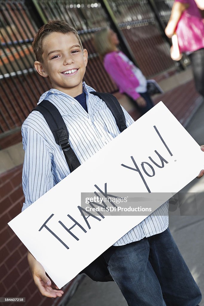 Heureux garçon tenant Merci de l'extérieur du bâtiment de l'école