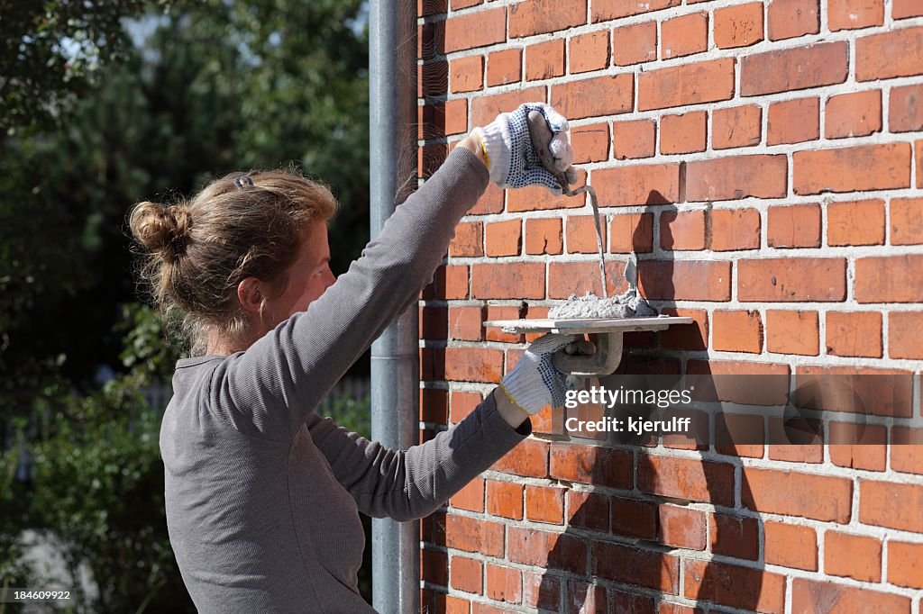 Female bricklayer cementing repairs on exterior house wall