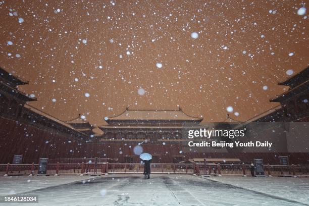 Citizen holding an umbrella stands at the Palace Museum during a snowfall on December 11, 2023 in Beijing, China. Beijing welcomes its first snow in...