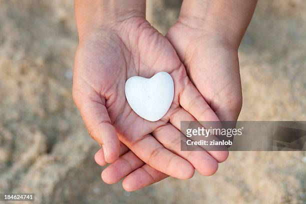 hands holding white heart-shaped pebble on the beach - love on the rocks stock pictures, royalty-free photos & images
