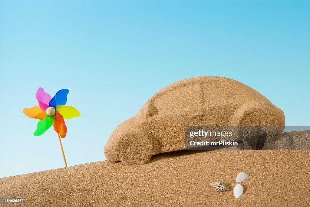 Sand sculpture of car beside toy windmill