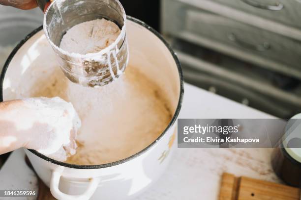 grind the flour in an iron calico mug over the pan with the dough. atmospheric photo of homemade baking, top view - powdered sugar sifter fotografías e imágenes de stock