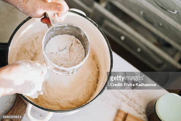 grind the flour in an iron calico mug over the pan with the dough. atmospheric photo of homemade baking, top view - powdered sugar sifter fotografías e imágenes de stock